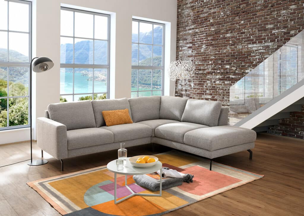 Ecksofa Bionda in grauer Stoffausführung mit kubischen Armlehnen.