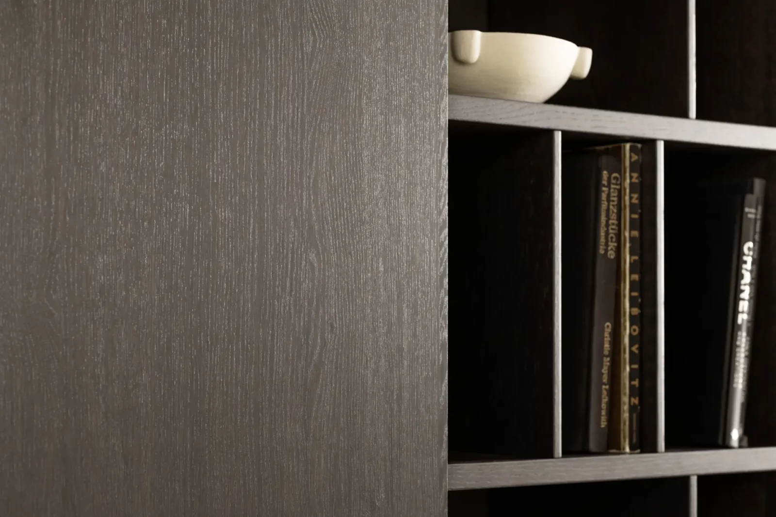 Dunkles Holzregal mit vertikalen Fächern, dekoriert mit Büchern und Schale.