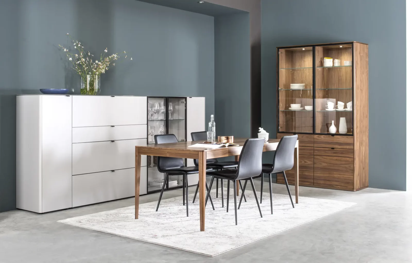 Esstisch aus Holz mit vier schwarzen Stühlen, Vitrine und Sideboard.