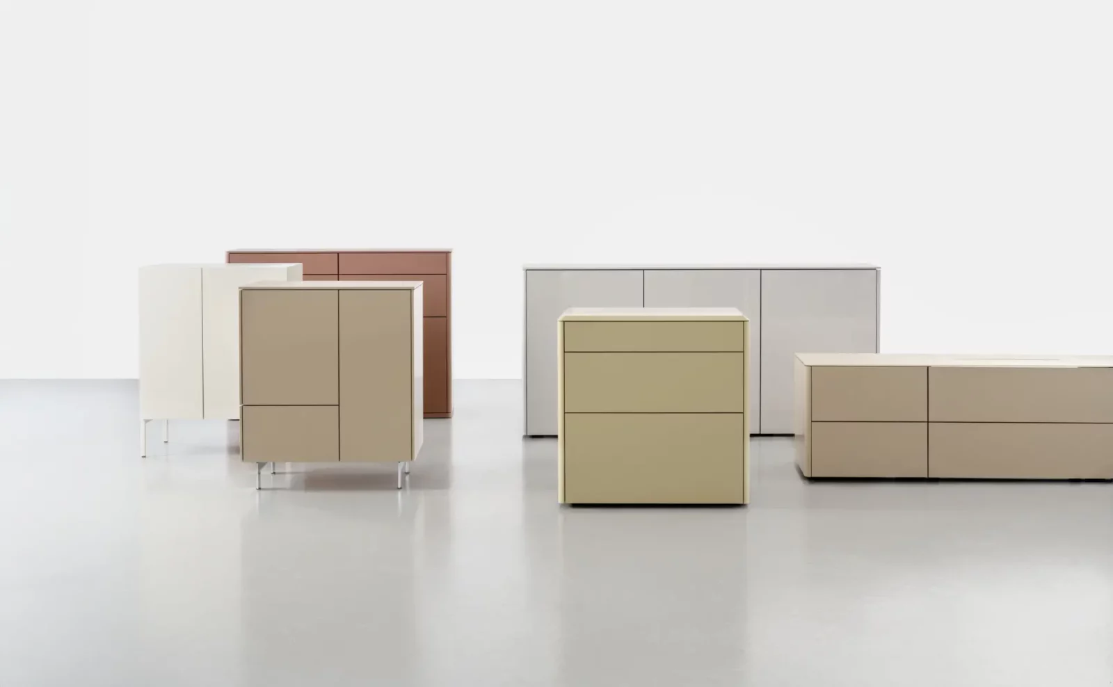 Verschiedene Gaya 090 Kommoden in Beige, Weiß und Braun auf grauem Boden.