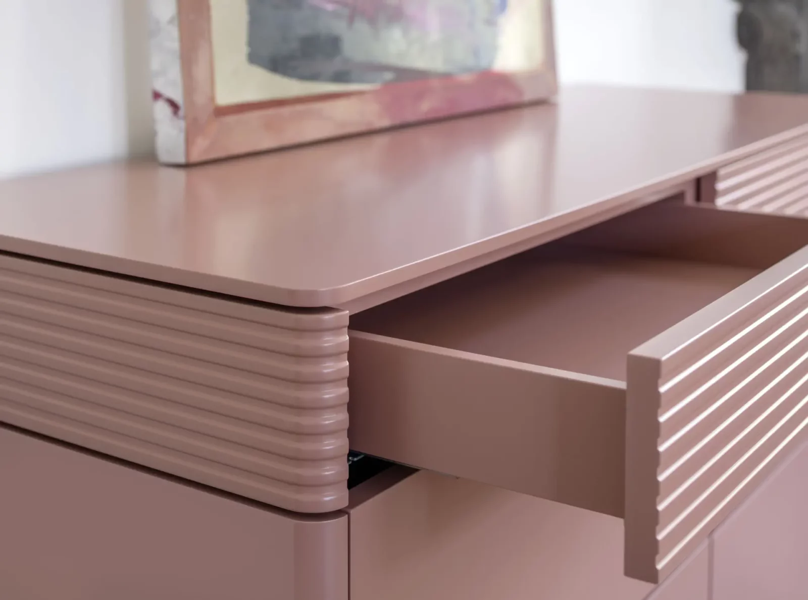 Kommode Gaya 104 in Rosa mit gerillten Fronten und offener Schublade.