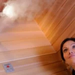 Eine Frau genießt entspannt den wohltuenden Dampf in einer exklusiven Sauna mit edler Holzverkleidung und moderner Steuerungseinheit.
