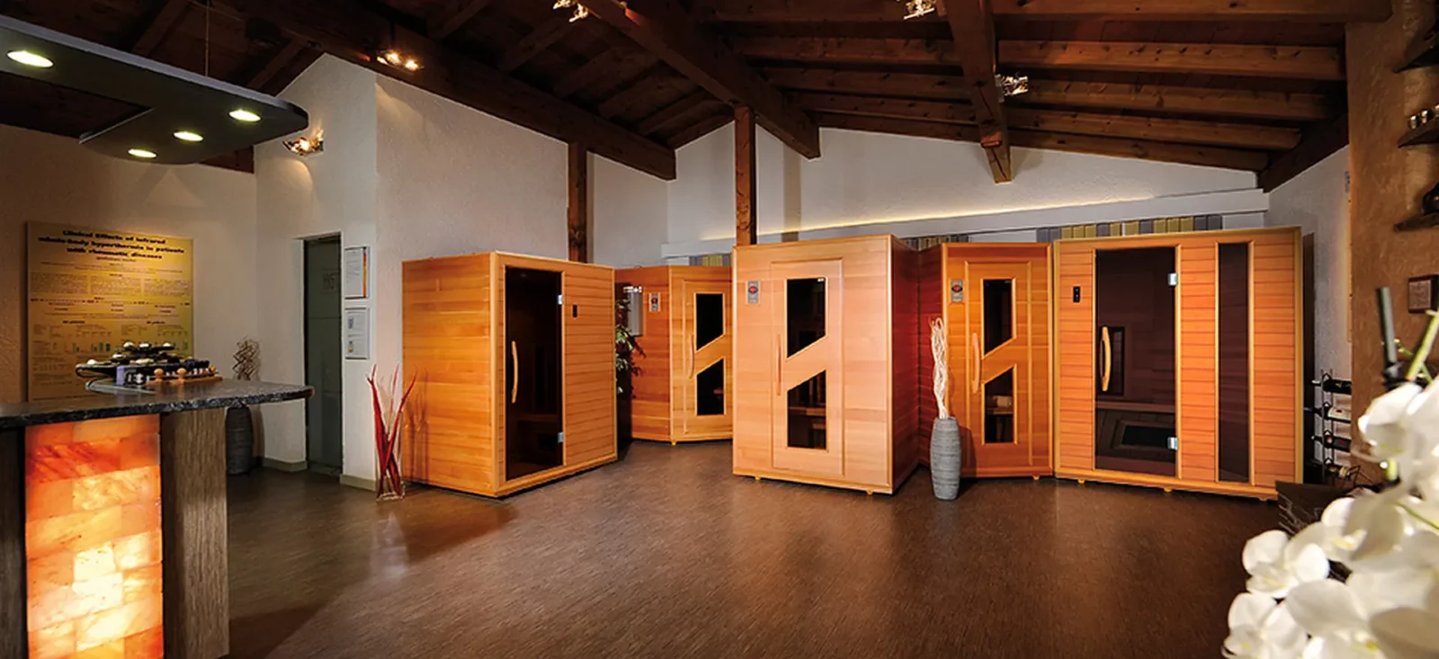 Mehrere hochwertige Infrarotkabinen aus hellem Holz in einem eleganten, warm beleuchteten Wellnessbereich mit einer Salzkristall-Theke.