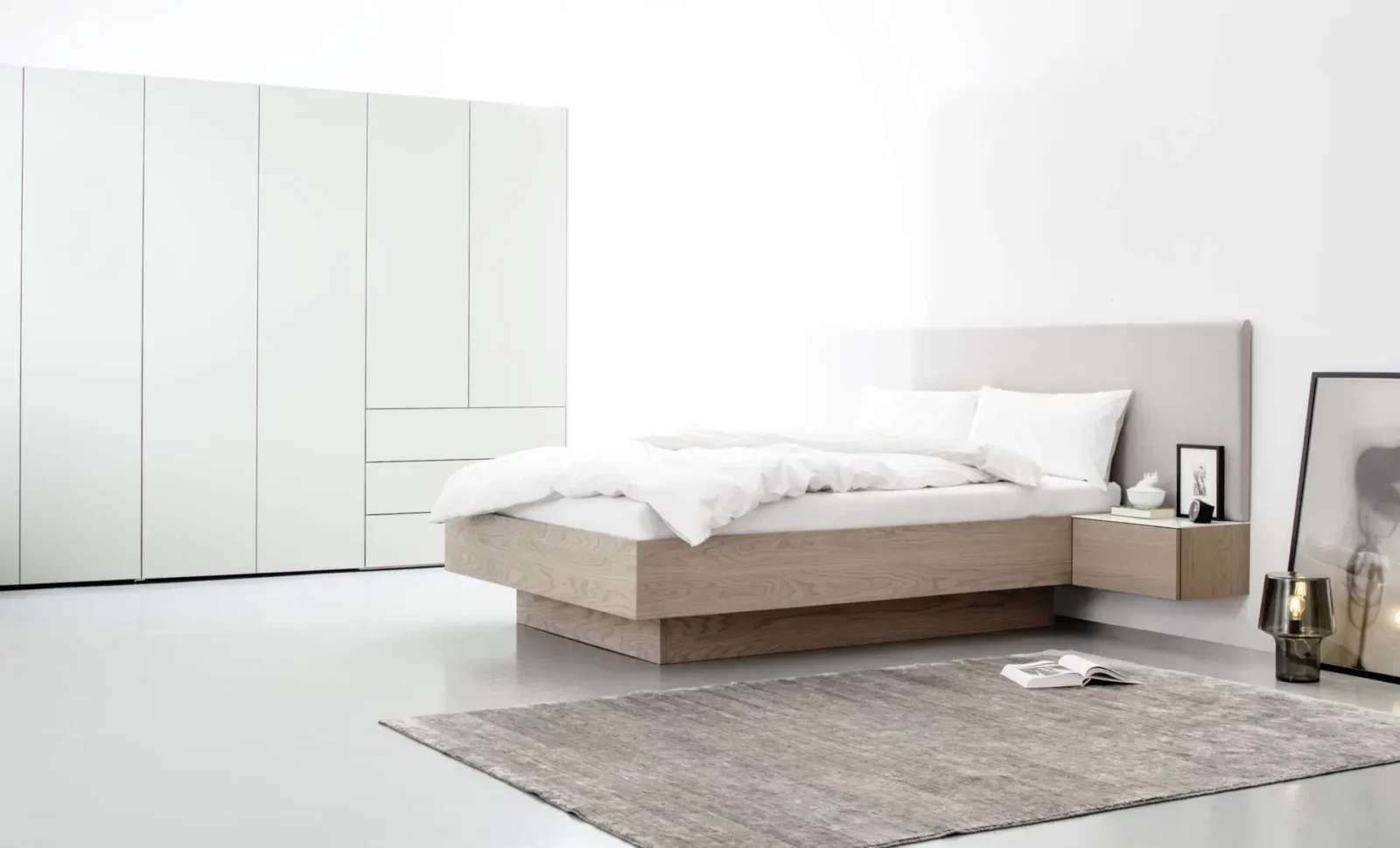Bett Maria 010 aus hellem Holz mit gepolstertem Kopfteil und integriertem Nachttisch.