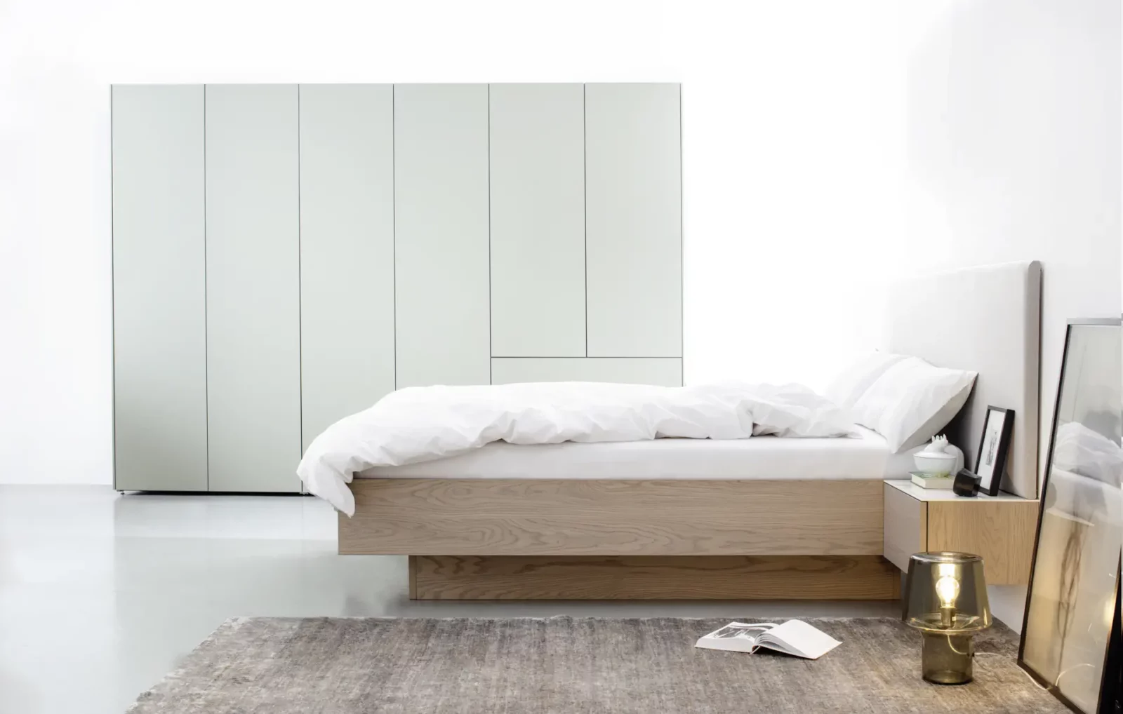 Bett aus hellem Holz mit gepolstertem Kopfteil und passendem Kleiderschrank.