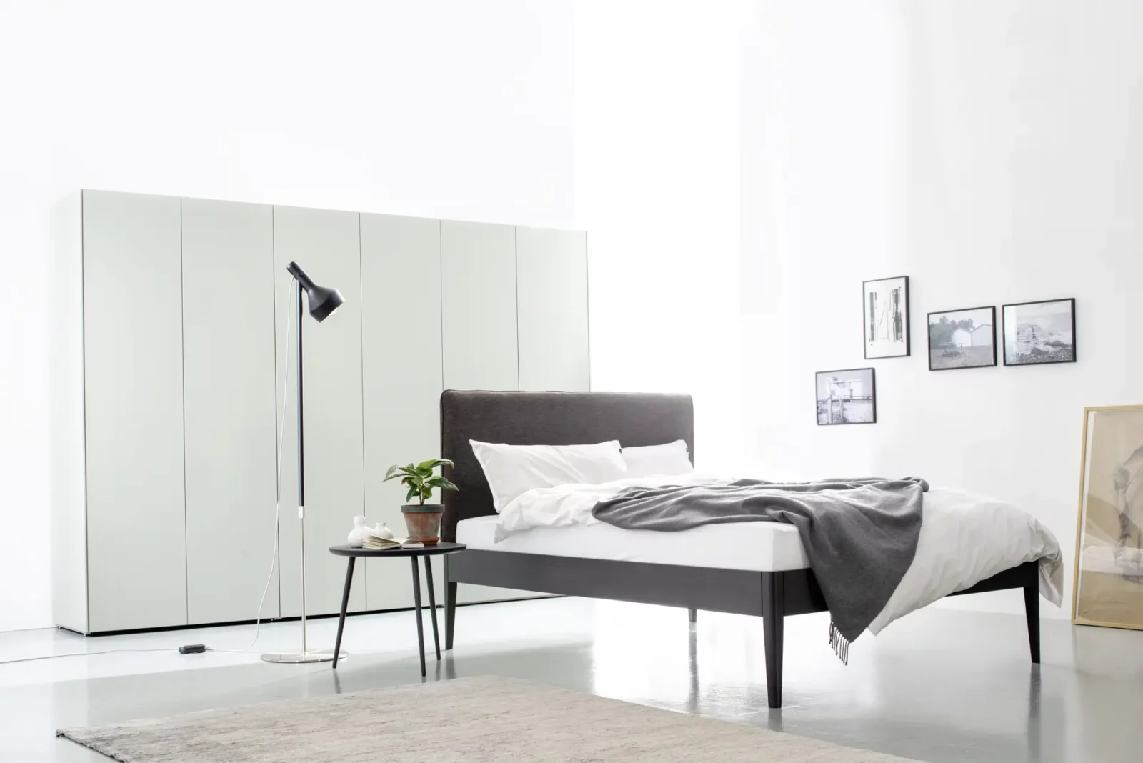 Bett Maria 016 mit dunklem Kopfteil und weißer Bettwäsche.