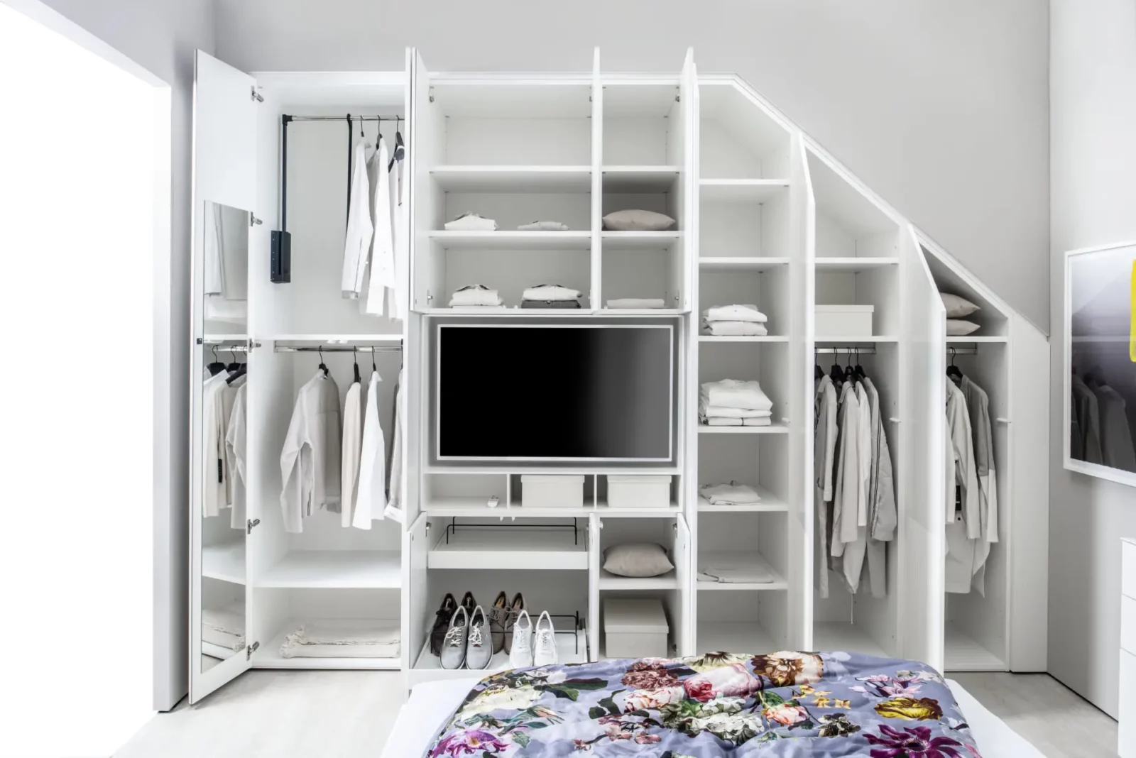 Weißer Einbauschrank mit TV, offenen Regalen und Kleiderstangen.