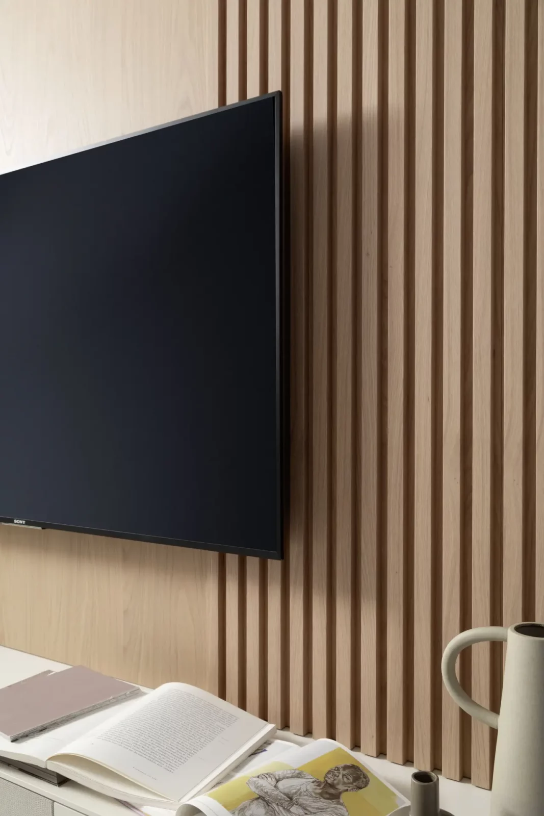 Holzverkleidete Wand mit vertikalen Lamellen, daneben ein moderner Flachbildfernseher.