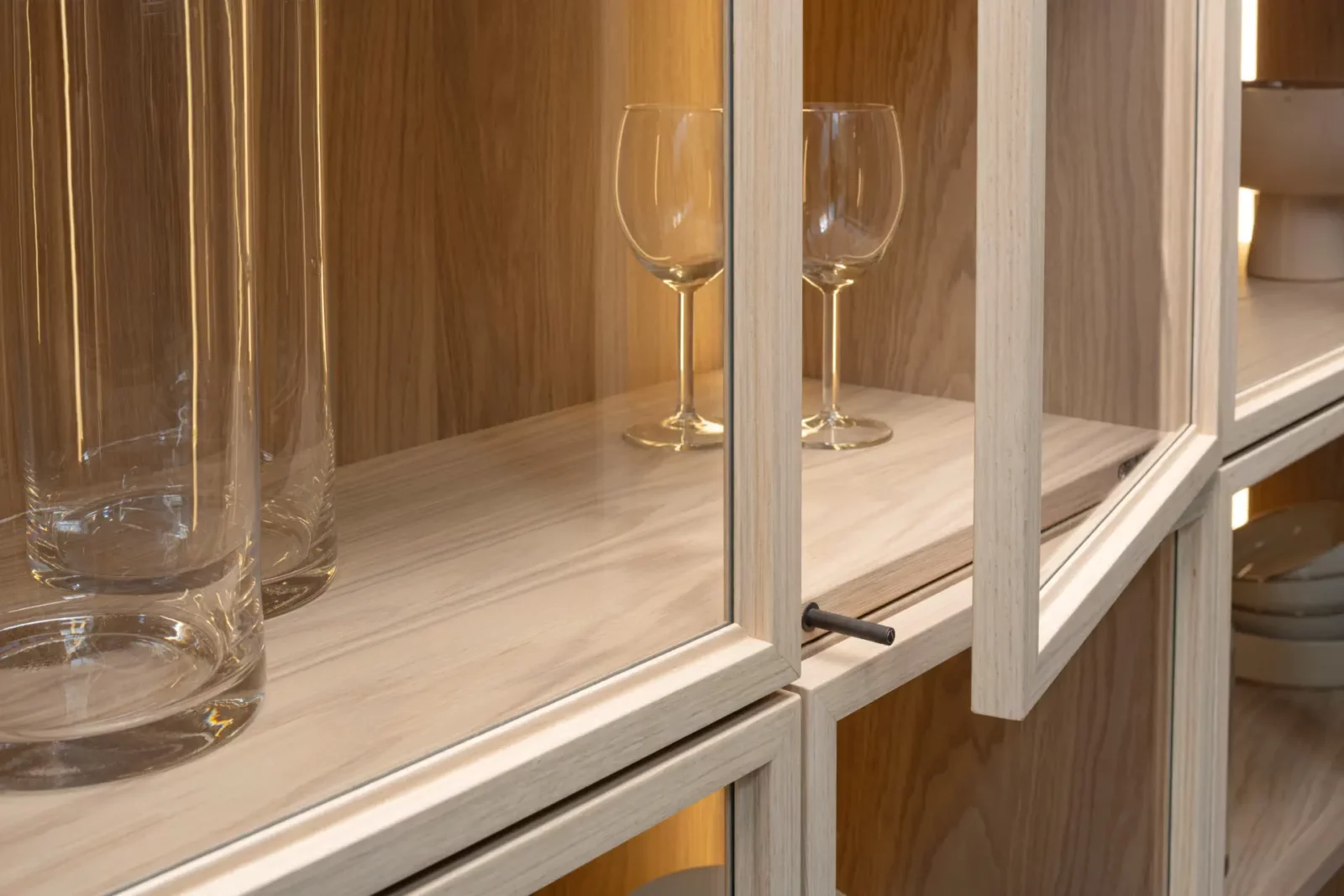 Vitrine Nubo 200 aus hellem Holz mit Glastüren und Metallgriff.