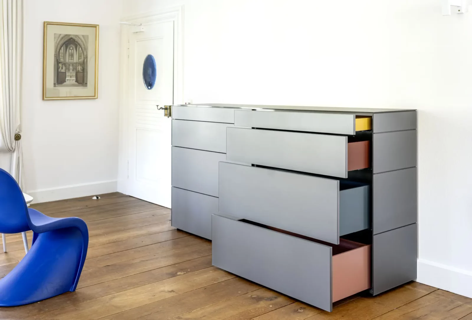 Graue Kommode Nubo 258 mit asymmetrischen Schubladen in verschiedenen Farben.