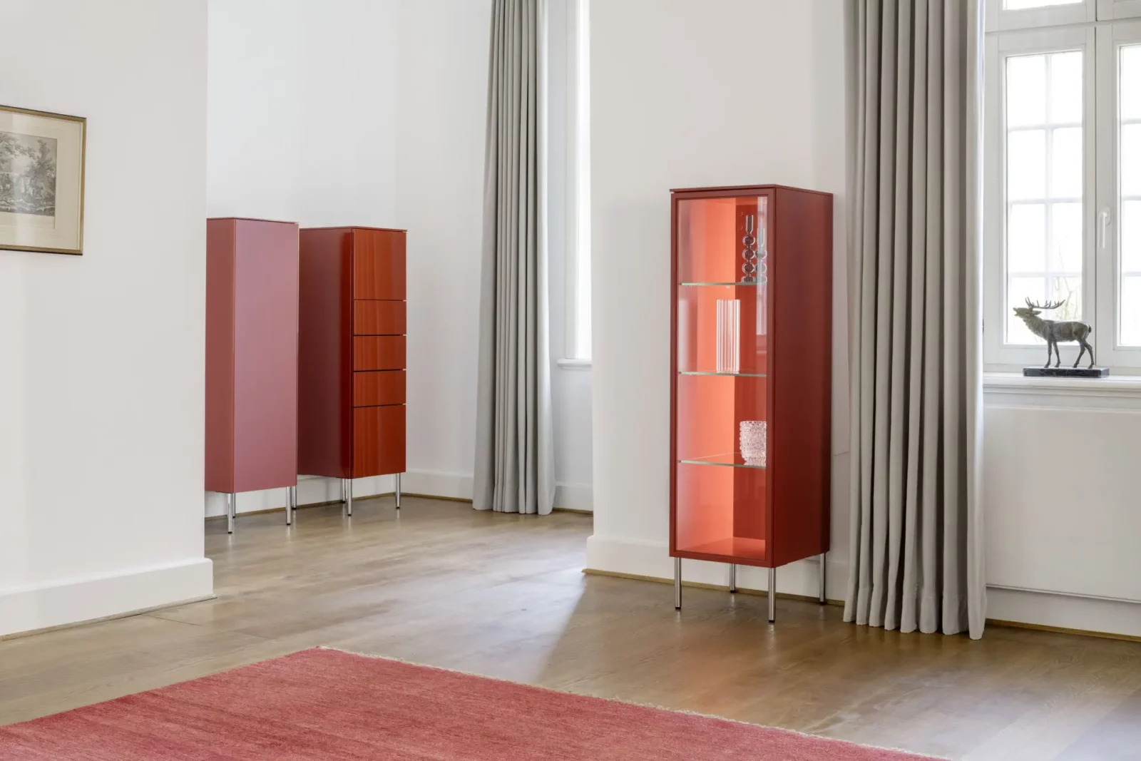 Vitrine Nubo 262, rot, mit Glasböden und Metallfüßen.