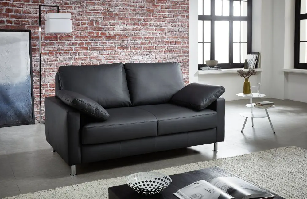 Schlafsofa Flexi in schwarzem Leder mit Metallfüßen und zwei Kissen.