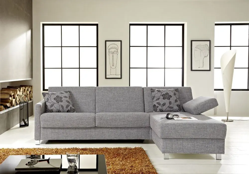 Schlafsofa Messida 11 in grauem Stoff mit floral gemusterten Kissen.