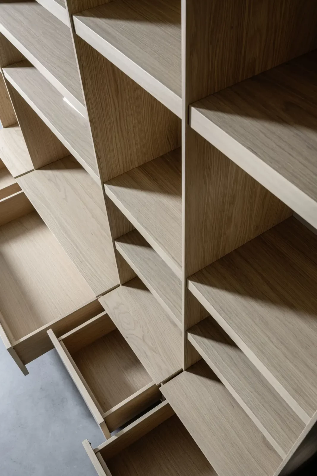 Regalwand Scalo 022 aus hellem Holz mit offenen Fächern und Schubladen.