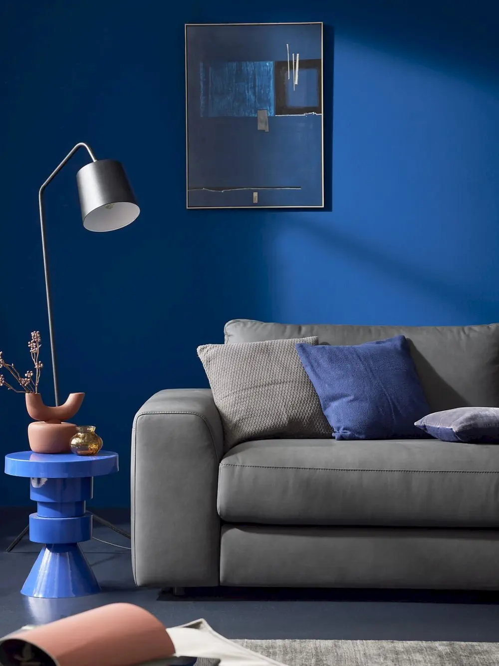 Sofa Gina in grauem Stoff mit blauen und grauen Kissen.