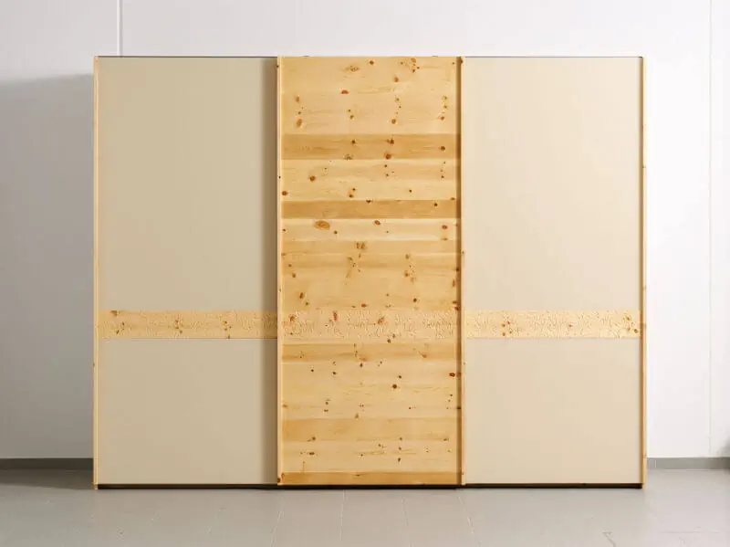 Schrank aus Zirbenholz mit Glasfronten und Latte-Design in Naturtönen.