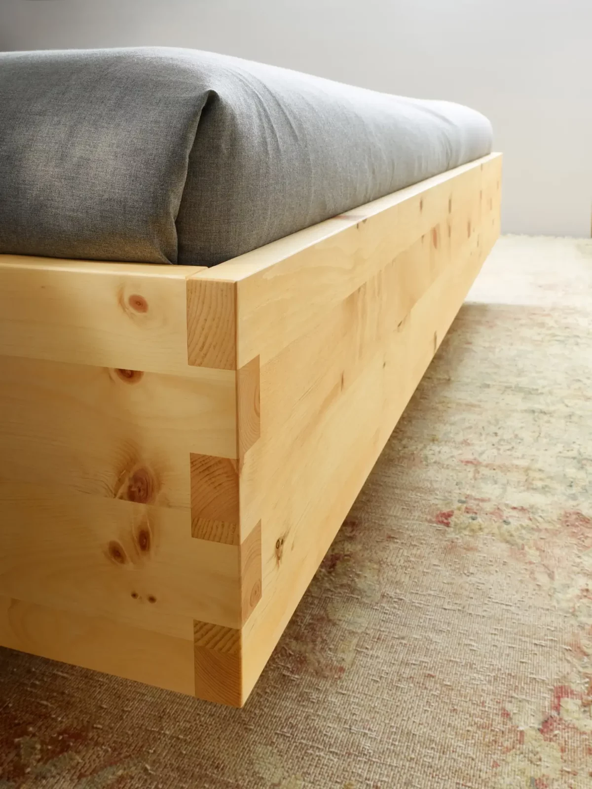 Anrei Paso Bett aus hellem Holz mit grauer Polsterung.