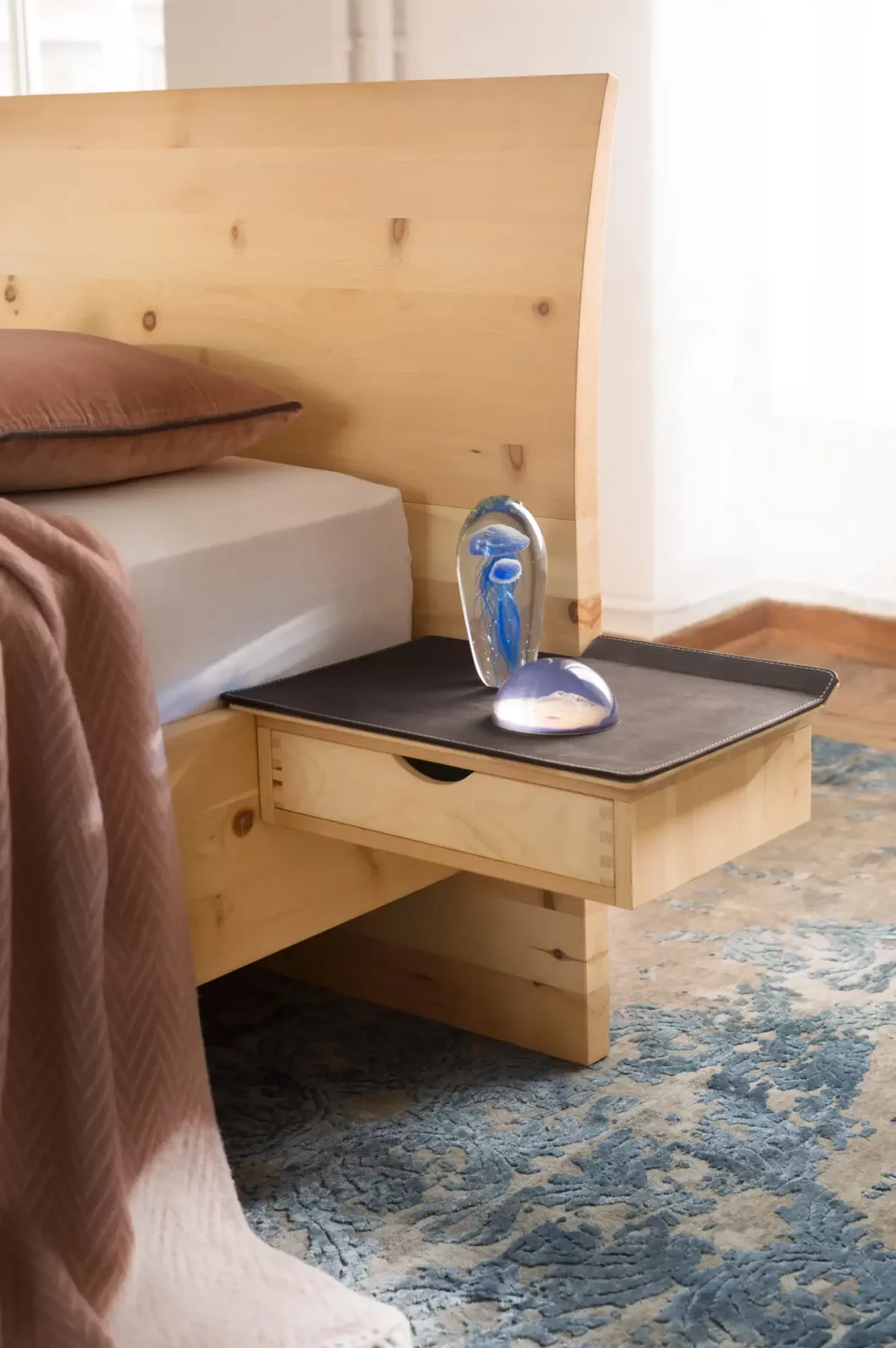 Anrei Paso Bett aus hellem Holz mit integriertem Nachttisch.