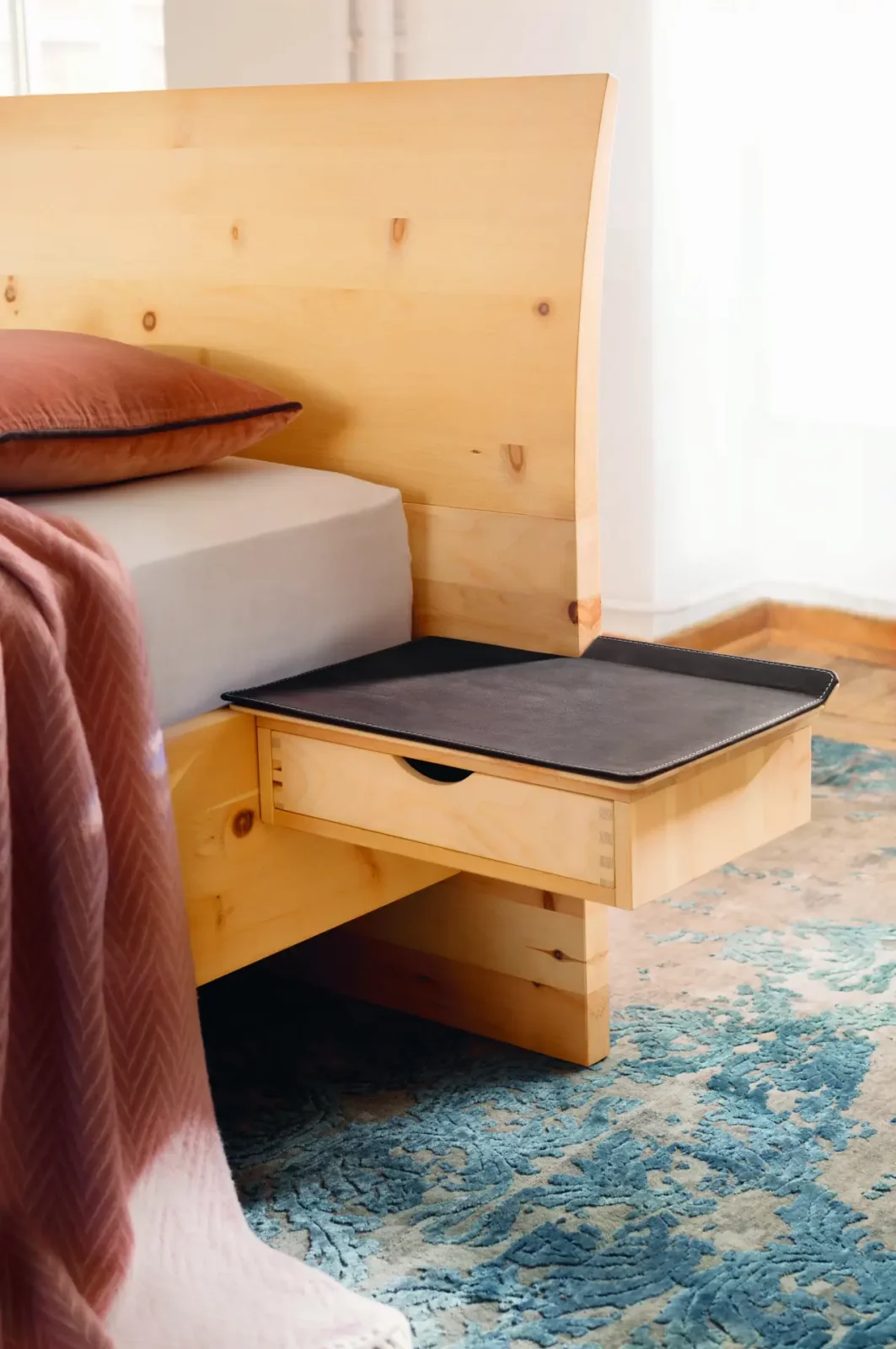Anrei Paso Bett aus hellem Holz mit integriertem Nachttisch.