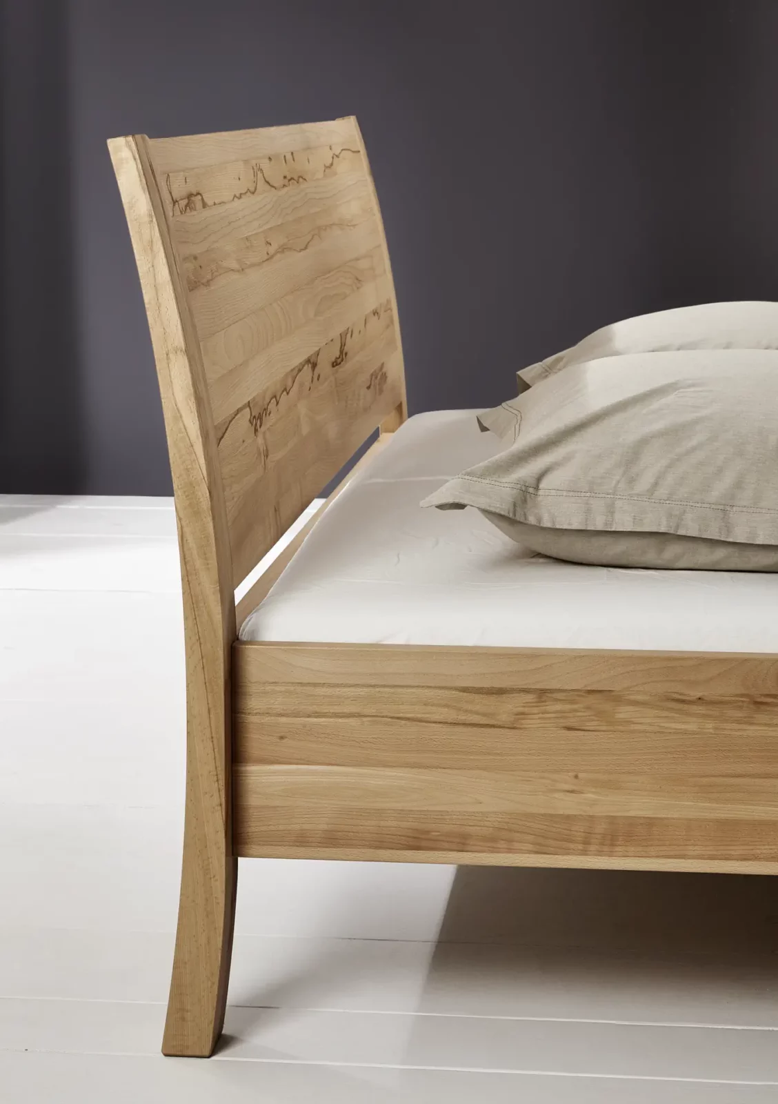 Holzschmiede Bett Swing aus hellem Holz mit geschwungenem Kopfteil.